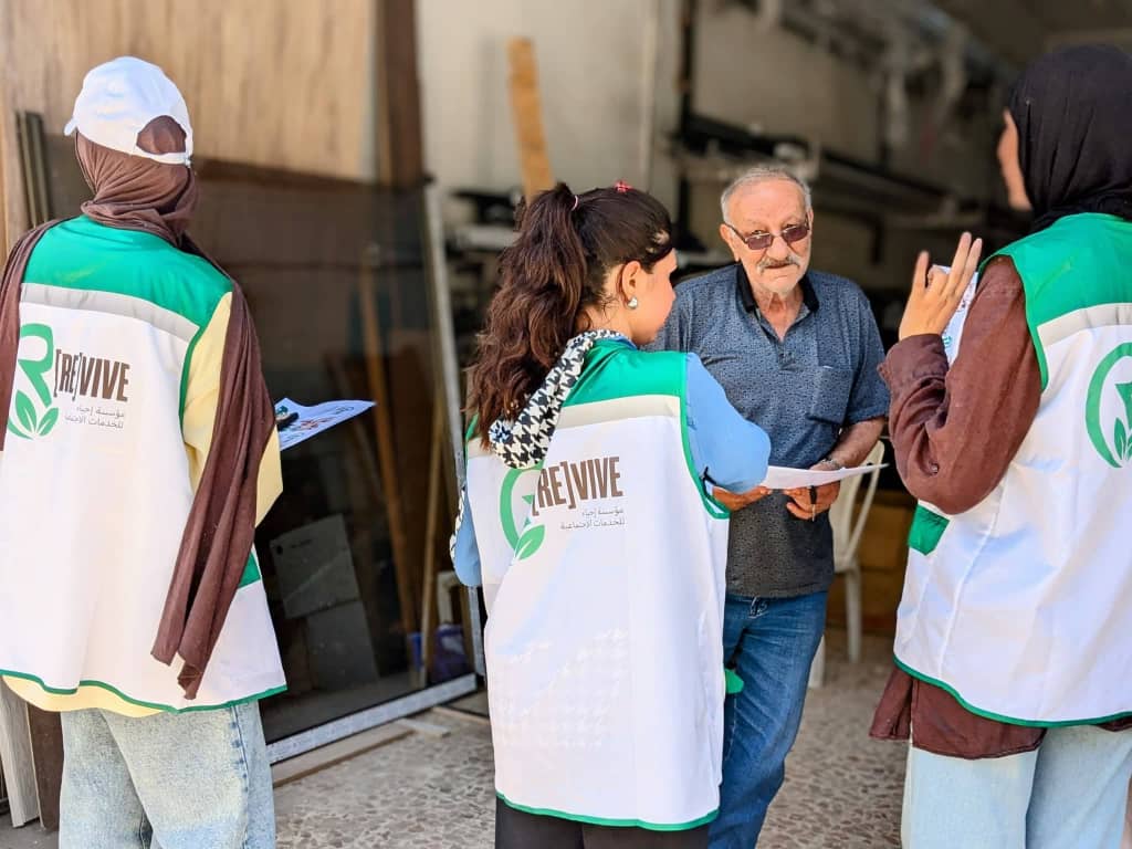 ثلاث متطوعات من مؤسسة إحياء بالسترات البيضاء والخضراء يتحدثن مع رجل من أهالي الحي